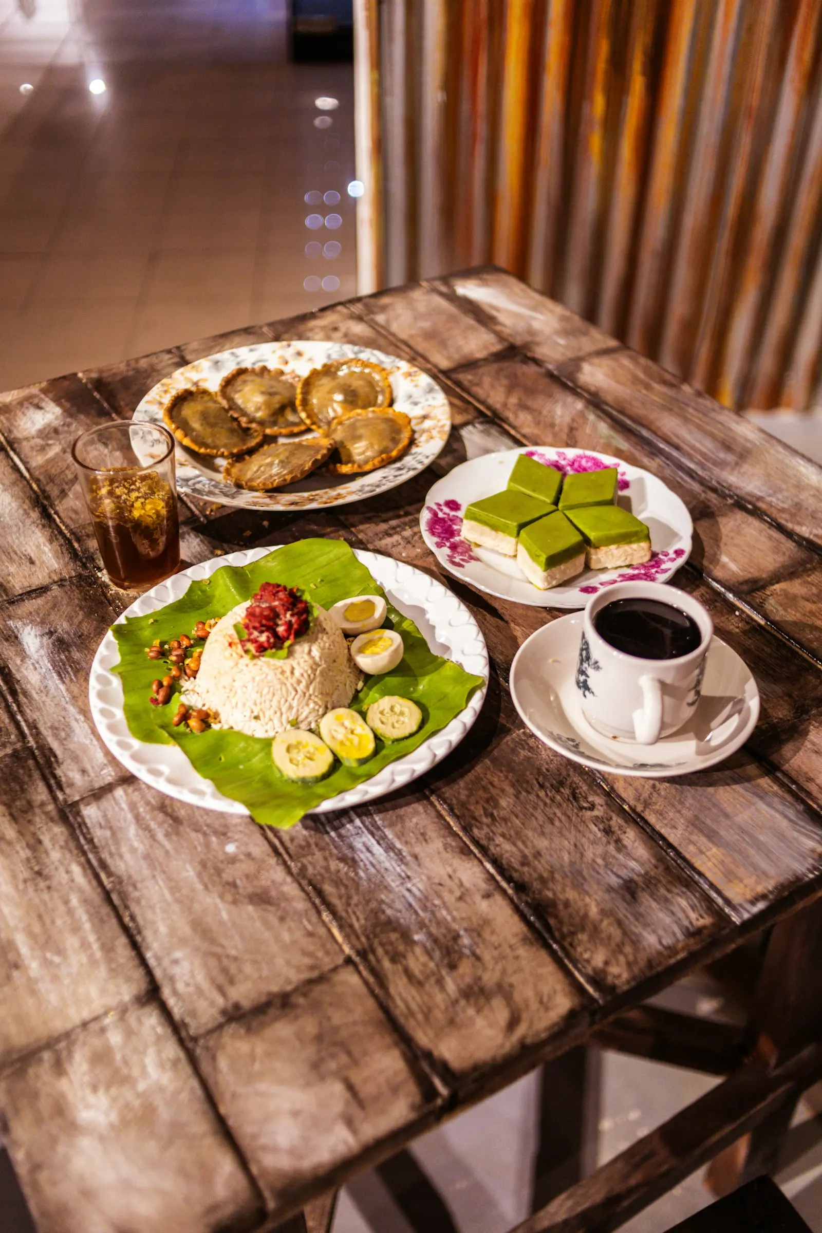 Nasi dengan lauk di atas daun pisang dan secangkir kopi di meja kayu